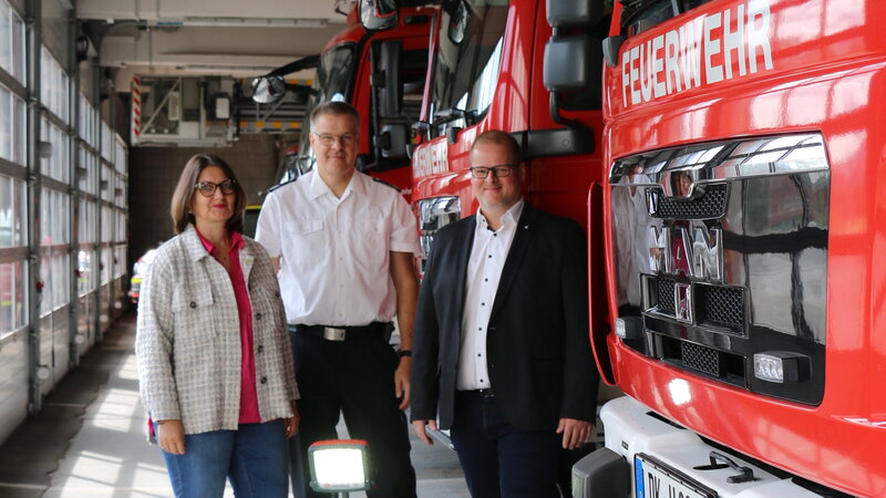 Bild von Spendenübergabe, drei Personen in der Fahrzeughalle der Feuerwehr