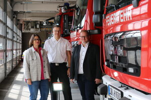 Bild von Spendenübergabe, drei Personen in der Fahrzeughalle der Feuerwehr