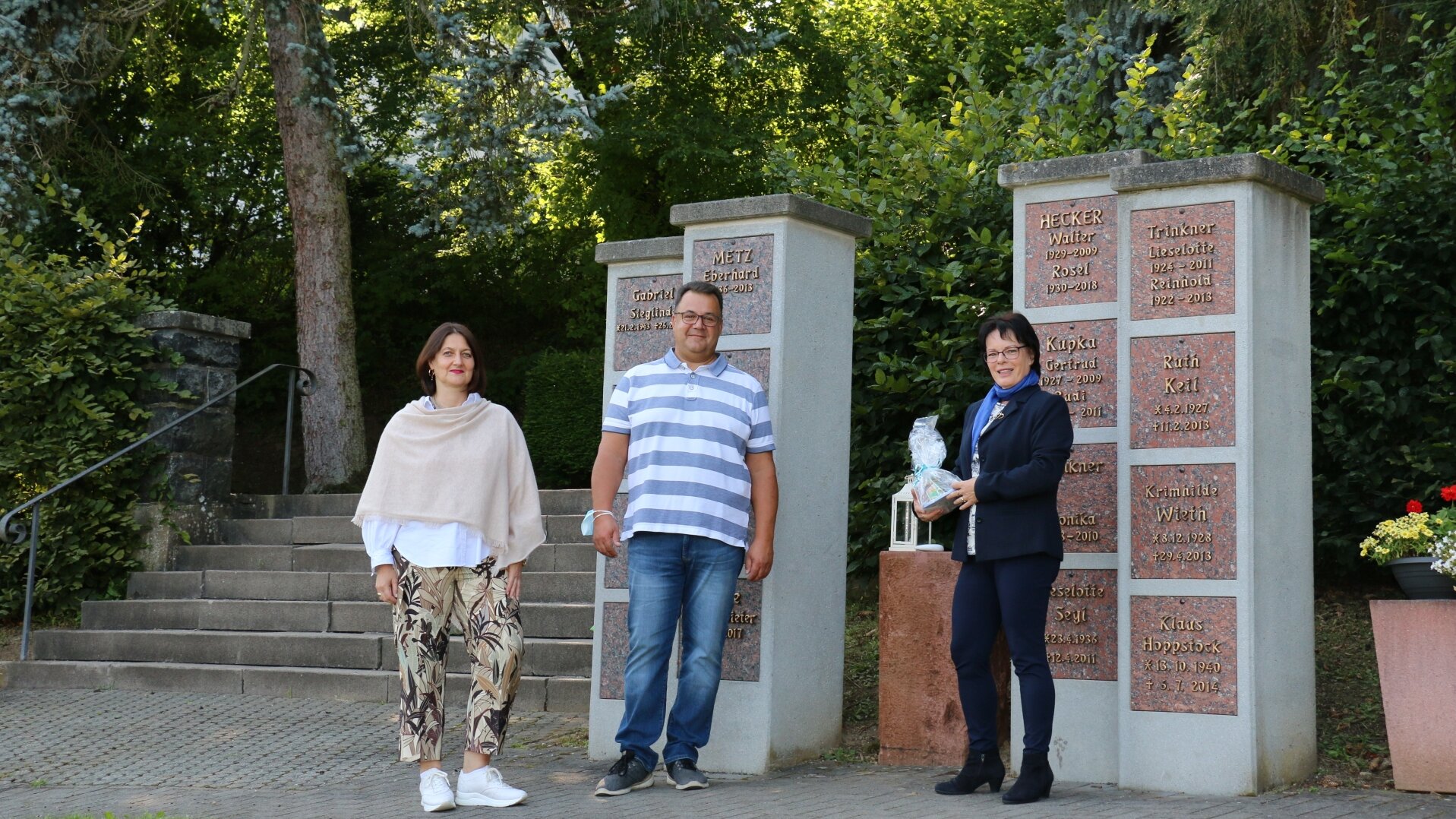 Drei Personen vor der Urnenwand auf dem Friedhof.