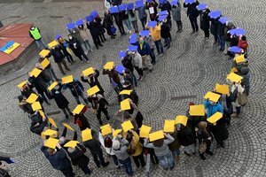 Peace-Zeichen mit Menschen, Menschen halten gelb-blaue Zettel als Zeichen der Solidarität mit der Ukraine empor.