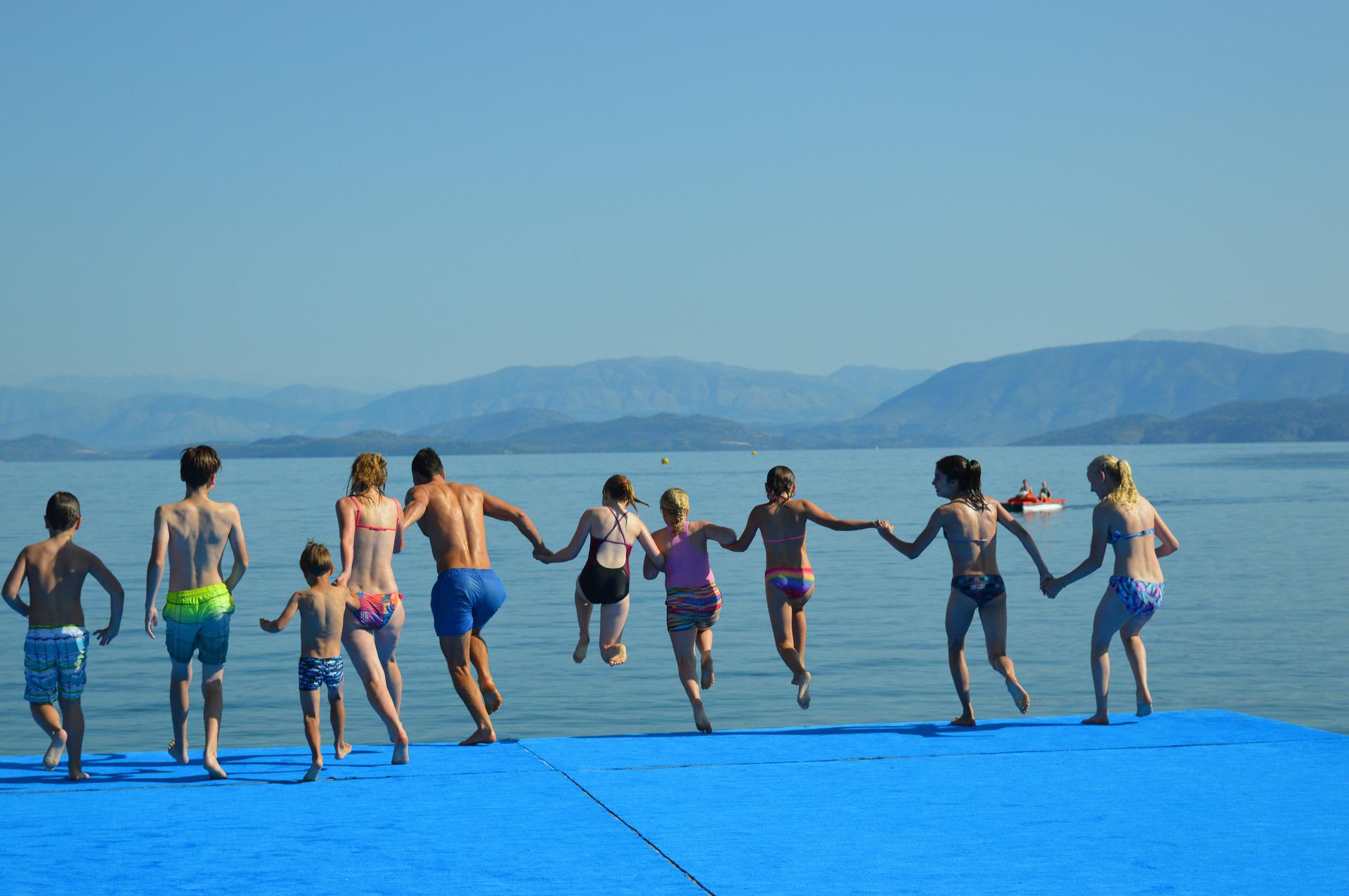 Kinder halten sich an der Hand und springen in einen See